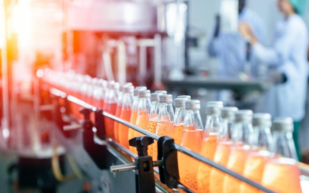 Filled bottles of orange drink travelling along a bottling line conveyor