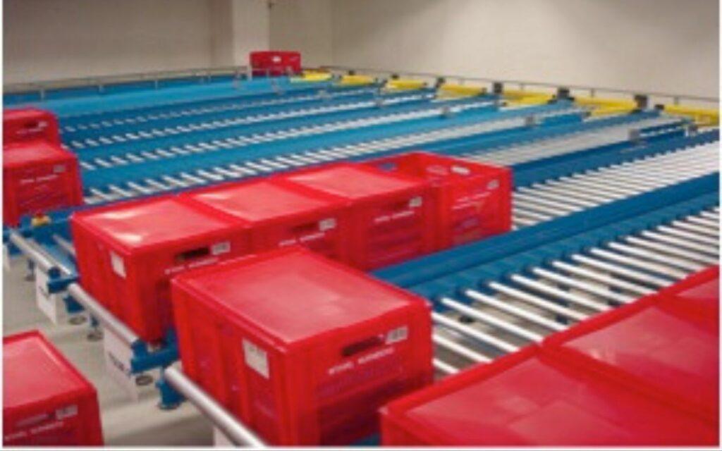 Red plastic totes travelling on gravity roller conveyor lanes in a distribution centre